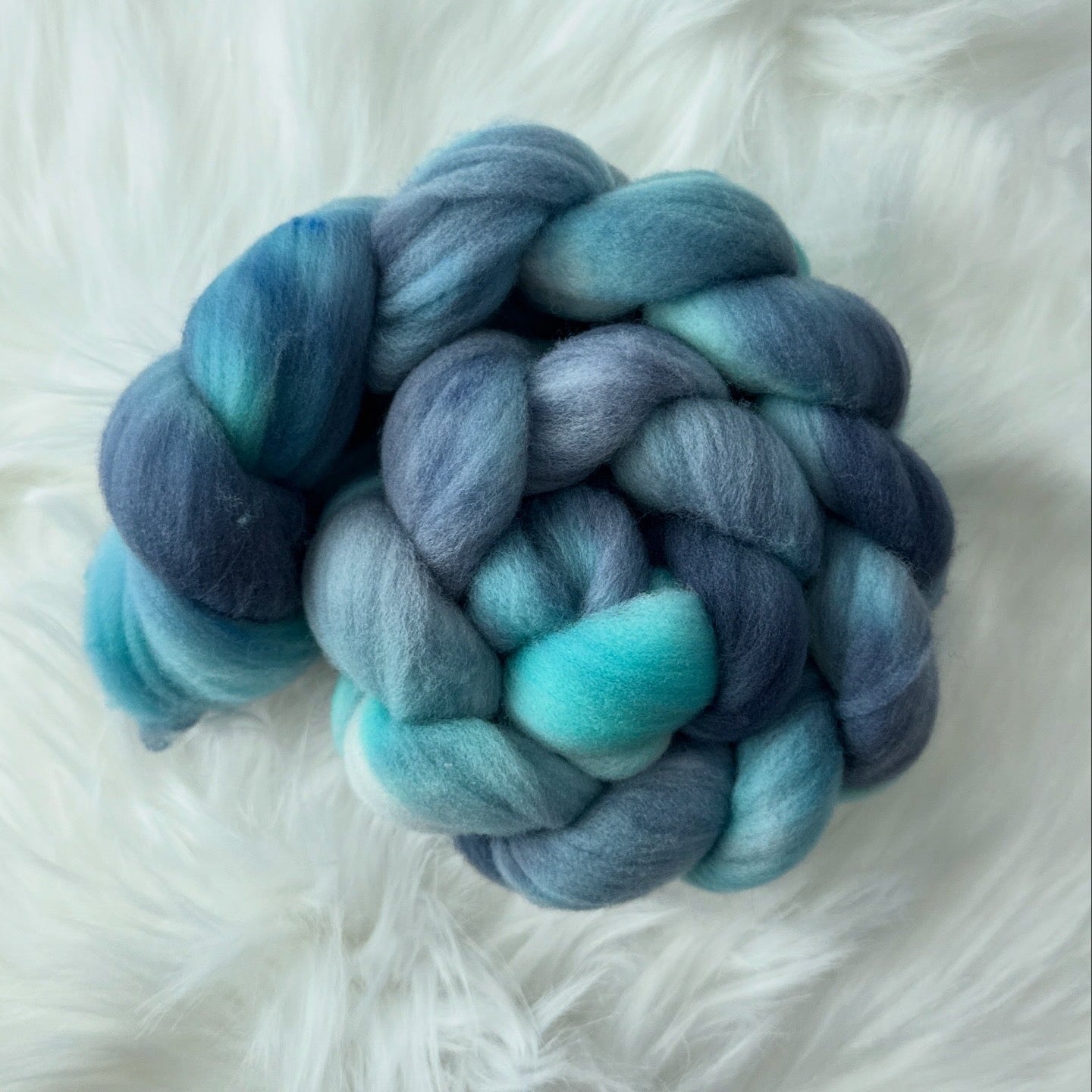 Braided skein of blue and green yarn on a white fluffy surface