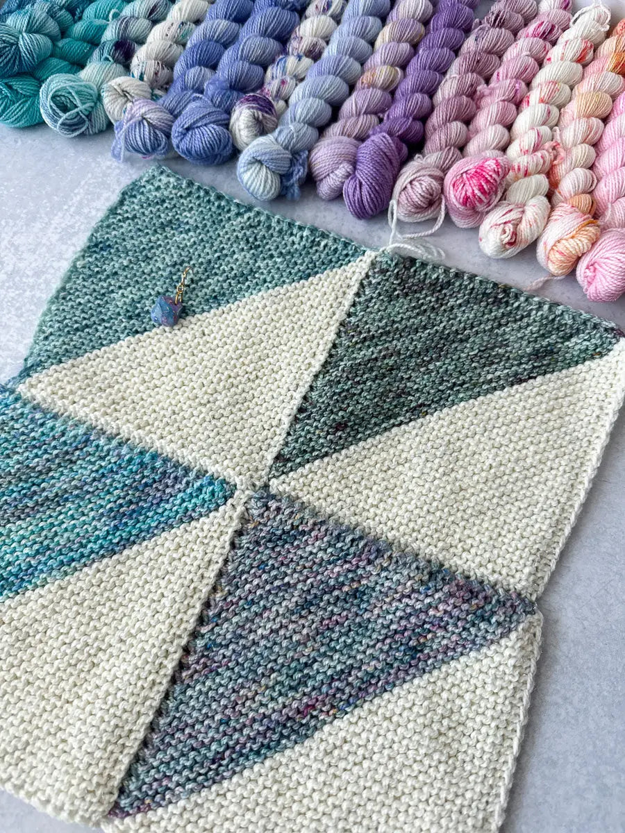 Knitted fabric with geometric pattern and colorful yarn skeins in the background